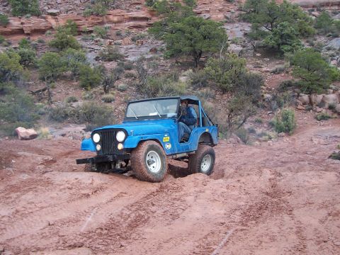 1991 Ford Bronco - A blue Jeep CJ-7 tackles a challenging muddy off-road course during the Moab Easter Jeep Safari.