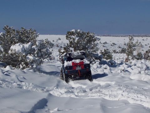 1991 Ford Bronco - A blue off-road vehicle navigates a snow-covered trail, carrying red gas cans.