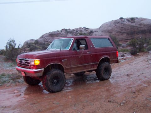 1991 Ford Bronco - A red 1992 Ford Bronco navigates a wet, muddy off-road trail.