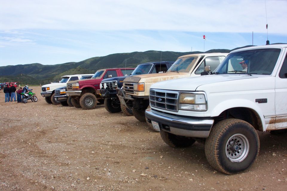 Row of lifted Ford Broncos and trucks parked on dirt, white one in foreground.