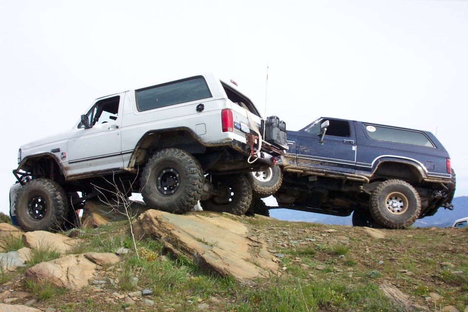 White and blue lifted Ford Broncos stacked on rock ledges showing extreme suspension flex