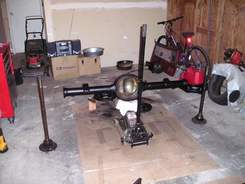 1986 Ford Bronco II - A rear axle assembly is shown on a jack, surrounded by various garage items including a bicycle and a lawnmower.