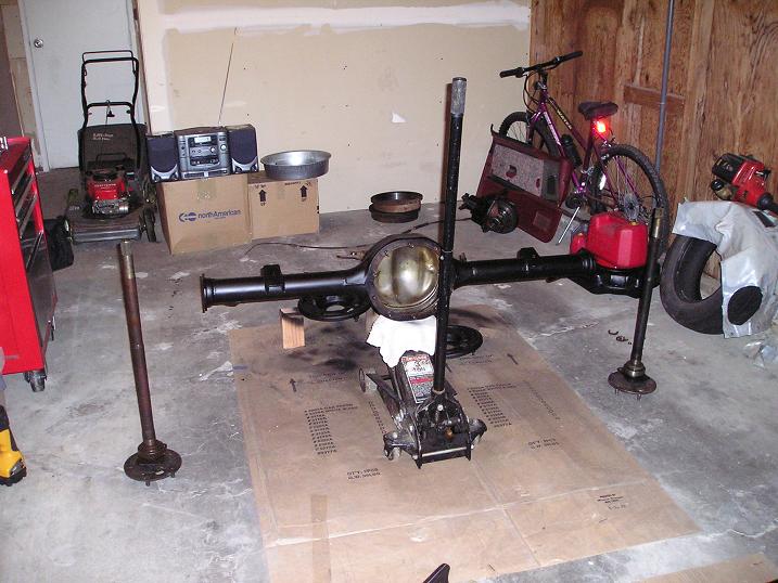 Rear axle assembly on a jack, with a bicycle and lawnmower in the background