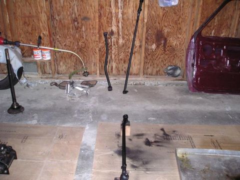 1986 Ford Bronco II - Car door and steering linkage parts laid out on a garage floor.
