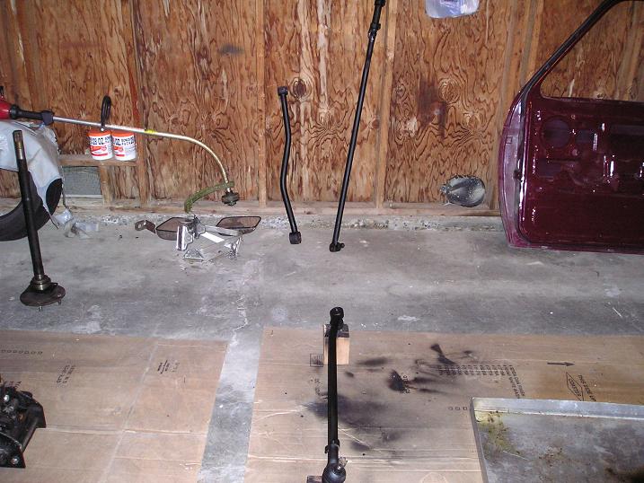 Three black fabricated steering and track bar links staged in a plywood-walled garage