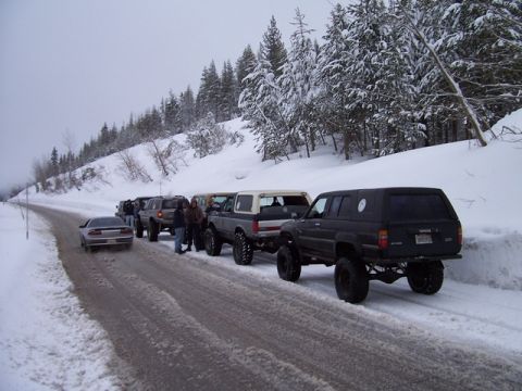 1989 Ford Bronco - A convoy of SUVs and a car are stopped on a snowy road in a wooded area.