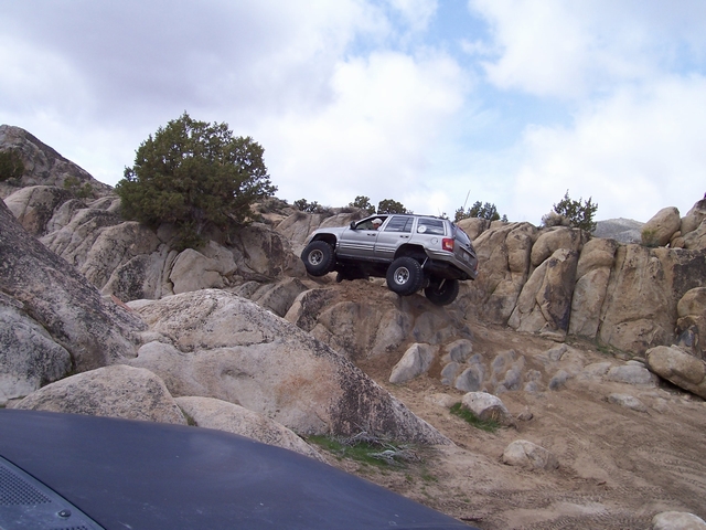 Silver Jeep Grand Cherokee climbing a granite rock ledge on off-road tires