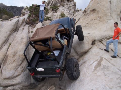 1989 Ford Bronco - An off-road vehicle navigates a steep rocky incline with two onlookers observing.