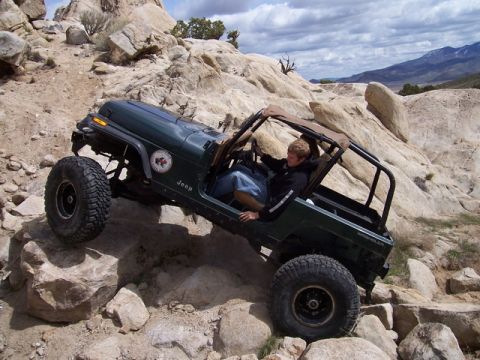 1989 Ford Bronco - A green Jeep Wrangler navigates a challenging rocky trail with a driver behind the wheel.