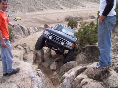 1989 Ford Bronco - A dark blue Ford Bronco is shown off-roading over large rocks in a desert-like environment.