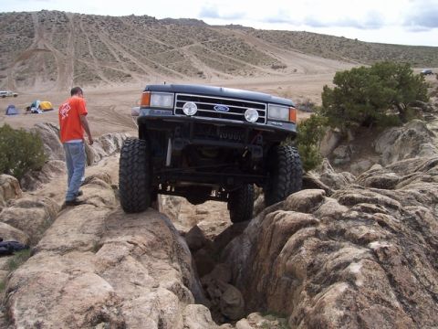 1989 Ford Bronco - This dark SUV, likely a 1987 model based on its grille, navigates a challenging rocky terrain.