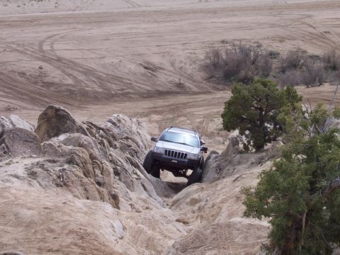 1989 Ford Bronco - A silver Jeep Grand Cherokee tackles a challenging rocky terrain on an off-road adventure.