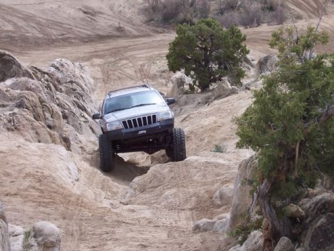 1989 Ford Bronco - Silver Jeep Grand Cherokee navigates a challenging rocky terrain during an off-road excursion.