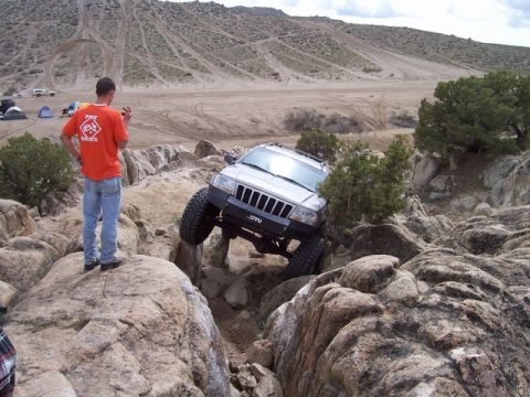 1989 Ford Bronco - A Jeep Grand Cherokee tackles a challenging rock crawl course with a spectator observing.