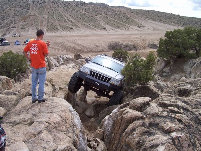 Silver Jeep Grand Cherokee navigating rocky terrain, front right tire high, driver watching