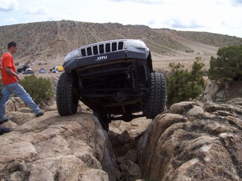 1989 Ford Bronco - A modified Jeep Grand Cherokee navigates a rocky obstacle course with spectators nearby.