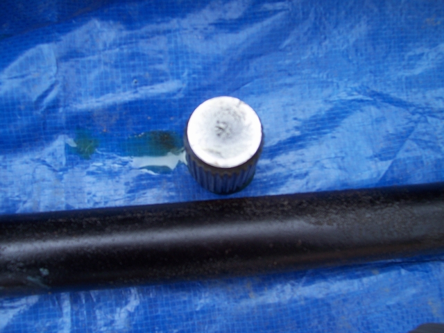 Metal cap with ribbed sides sits on a black pipe, both on a blue tarp