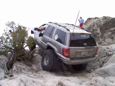 1989 Ford Bronco - A silver Jeep Grand Cherokee navigates a rocky off-road trail with two people observing.