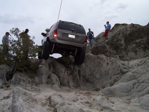 1989 Ford Bronco - An SUV with significant suspension modifications tackles a challenging rocky trail, with onlookers observing the difficult maneuver.