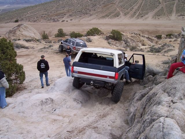 Rear of lifted blue and white Ford Bronco descending white rock ledge in desert