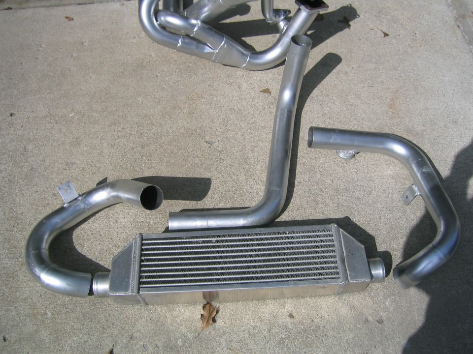 Intercooler and piping kit on concrete. Includes silver-colored metal tubes and a finned intercooler