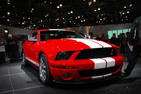 2005 Ford Mustang - A red Ford Mustang Shelby GT500 is displayed indoors with people watching.