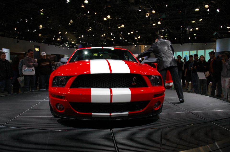 Red 2005 Ford Mustang with dual white racing stripes and a Cobra emblem on the grille, viewed from the front