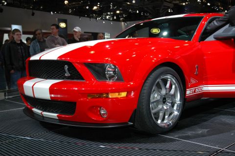 2005 Ford Mustang - This red 2005 Ford Mustang GT 500 features iconic white racing stripes and a prominent grille emblem.