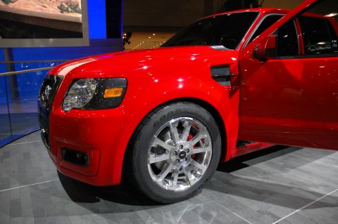 2005 Ford Mustang - This red SUV, likely a 2005 model, is displayed with its door open, its chrome wheels and performance tires.