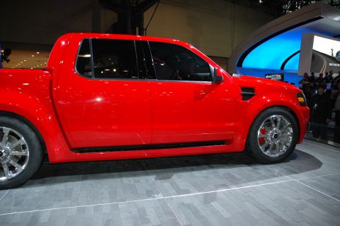2005 Ford Mustang - A bright red pickup truck is displayed at an auto show, its side profile and custom wheels.