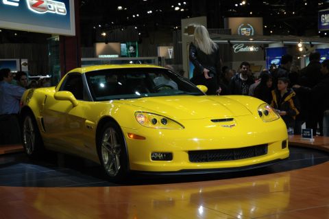 2005 Ford Mustang - A yellow Chevrolet Corvette C6 is displayed at an auto show with spectators in the background.