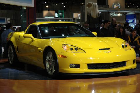 2005 Ford Mustang - A bright yellow Chevrolet Corvette is showcased at an auto show with people in the background.