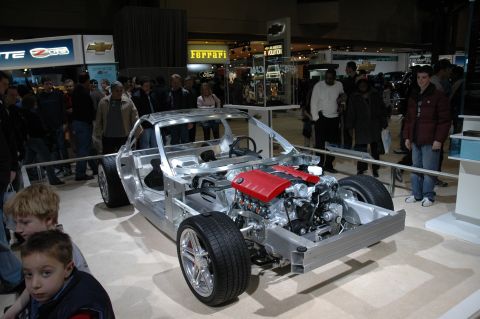 2005 Ford Mustang - A car's chassis and engine are displayed at an auto show, with onlookers in the background.