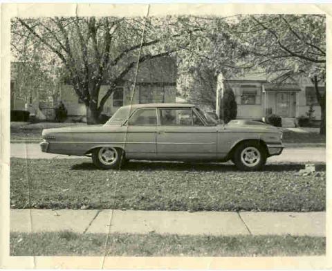1963 Ford Galaxie - A 1963 Ford Galaxie sedan with a hood scoop is parked on a grassy lawn in front of houses.