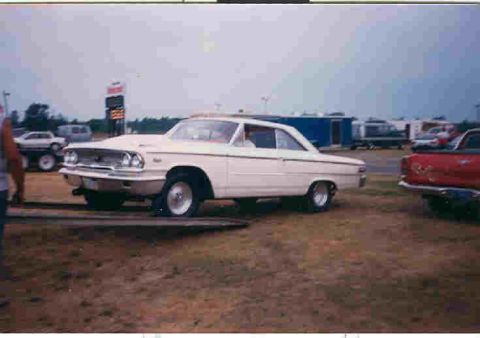 1957 Ford Deluxe - A white 1963 Ford Galaxie coupe is positioned on a trailer at an outdoor event.