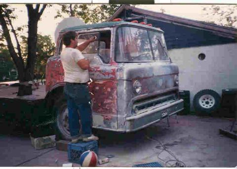 1957 Ford Deluxe - A man works on the front of a truck that appears to be undergoing restoration or repair.