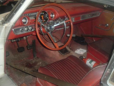 1963 Ford Galaxie - The interior of a vintage car shows red upholstery, a large steering wheel, and a fire extinguisher on the passenger seat.