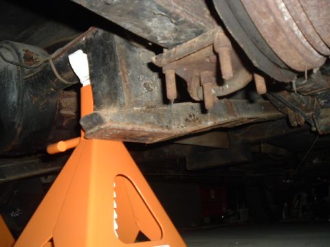 1963 Ford Galaxie - The underside of a vehicle is shown, supported by orange jack stands, revealing rusty metal components and suspension parts.