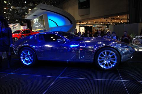 2005 Ford Mustang - A shiny, futuristic concept car is showcased with blue lighting, while a red truck is visible behind it.