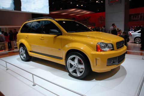 2005 Ford Mustang - A yellow SUV is showcased at an auto exhibition with other vehicles and people in the background.