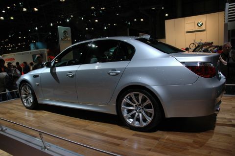 2005 Ford Mustang - A silver BMW sedan is displayed indoors on a wooden platform, viewed from the rear three-quarter angle.