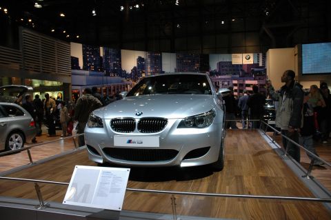 2005 Ford Mustang - A silver BMW M5 sedan is displayed at an auto show with people around.