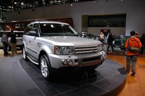 2005 Ford Mustang - A silver Range Rover is displayed on a platform at an auto show, with people milling around in the background.