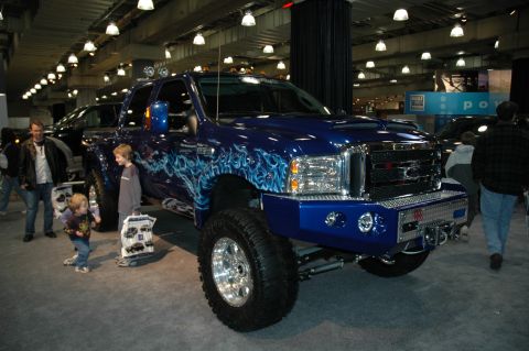 2005 Ford Mustang - A modified blue Ford F-250 pickup truck is displayed indoors, custom flame decals and a large chrome bumper.