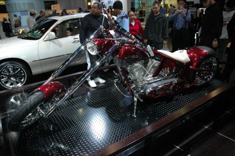 2005 Ford Mustang - A custom chopper motorcycle is displayed next to a white sedan at an indoor event.