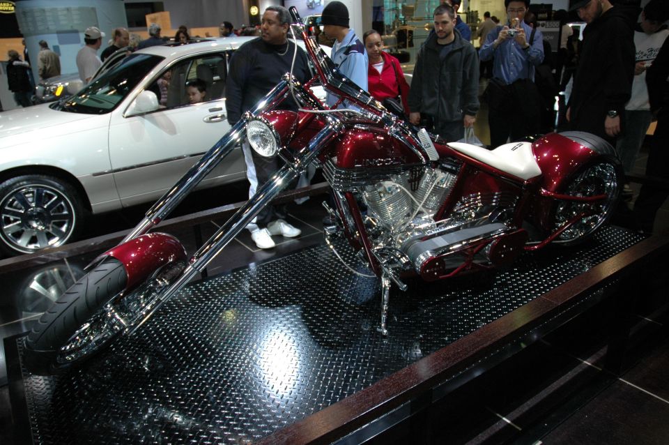 Red custom chopper motorcycle with white seat and chrome accents, viewed from the front-right