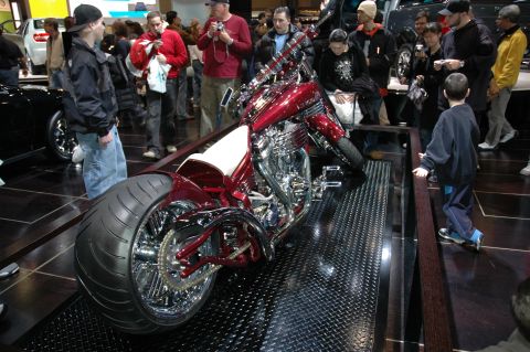 2005 Ford Mustang - A custom chopper motorcycle is displayed indoors with onlookers observing.