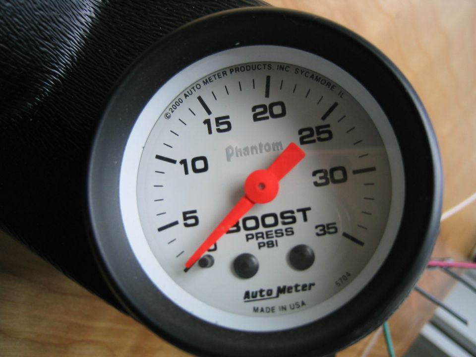 Auto Meter boost pressure gauge with red needle and white face, reading approximately 5 PSI