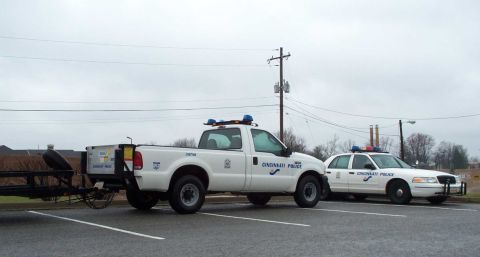 1998 Ford Crown Victoria - Two Cincinnati Police vehicles, a pickup truck and a Crown Victoria, are parked in a lot under an overcast sky.