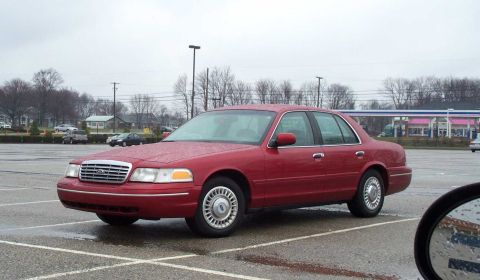 1998 Ford Crown Victoria - Red 1998 Ford Crown Victoria sedan parked in an empty lot under an overcast sky.